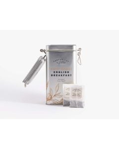Open silver tin with metal clasp of Cartwright & Butler English breakfast tea, with illustrations of leaves in brown. In front of the tin is two teabags 
