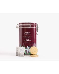 Dark red tin with metal clasp of Cartwright & Butler tea for two selection with illustrations of flowers in white, red, and pink as well as a teapot. In front of the tin is two teabags and two biscuits leaning against the tin 