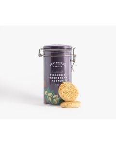 Dark purple tin with metal clasp of Cartwright & Butler pistachio shortbread rounds with illustrations of different flowers and some pistachios in different shades of green, orange, and pink. There are two biscuits in front of the tin
