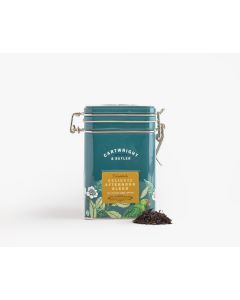 Dark blue tin with metal clasp of Cartwright & Butler delicate afternoon blend with colourful illustrations of flowers, leaves, and a bird. With a small amount of tea placed in front of the tin