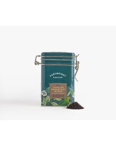 Dark blue tin with metal clasp of Cartwright & Butler English breakfast blend with colourful illustrations of flowers, leaves, and a bird. With a small amount of tea blend placed in front of the tin