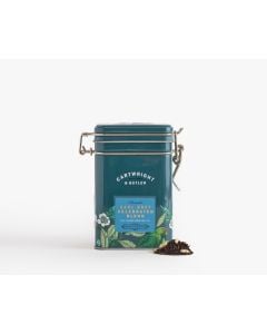 Dark blue tin with metal clasp of Cartwright & Butler earl grey celebrated blend with colourful illustrations of flowers, leaves, and a bird. With a small amount of tea blend placed in front of the tin