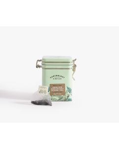 Light green tin with metal clasp of Cartwright & Butler English breakfast blend tea with colourful illustrations of flowers, leaves, and a bird. With a tea bag placed in front 