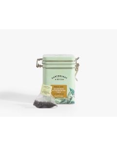 Light green tin with metal clasp of Cartwright & Butler classic afternoon tea with colourful illustrations of flowers, leaves, and a bird. With a tea bag placed in front of the tin