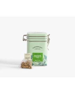 Light green tin with metal clasp of Cartwright & Butler delicate camomile tea with colourful illustrations of flowers, leaves, and a bird. With a tea bag placed in front of the tin