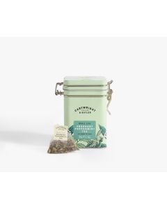 Light green tin with metal clasp of Cartwright & Butler fragrant peppermint tea with colourful illustrations of flowers, leaves, and a bird. With a tea bag placed in front of the tin