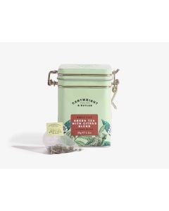 Light green tin with metal clasp of Cartwright & Butler whole leaf green tea with citrus blend with colourful illustrations of flowers, leaves, and a bird. With a tea bag placed in front of the tin
