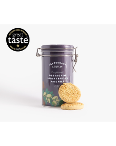 Dark purple tin with metal clasp of Cartwright & Butler pistachio shortbread rounds with illustrations of different flowers and some pistachios in different shades of green, orange, and pink. There are two biscuits in front of the tin
